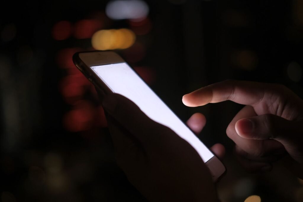 Mãos segurando celular no escuro, ilustrando a dúvida se uma bet chinesa é confiável